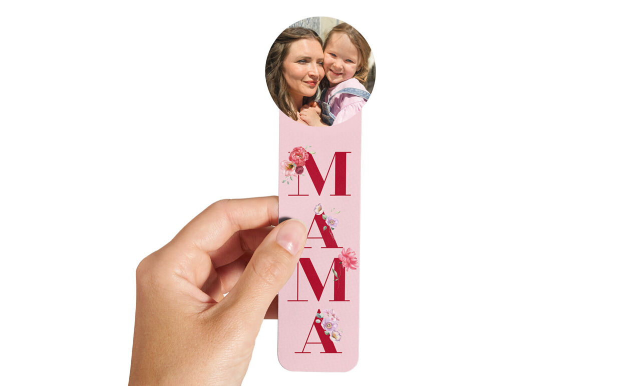 Marcapáginas rosa personalizado con texto 'MAMÁ' y foto circular de una madre con su hija, sostenido en una mano